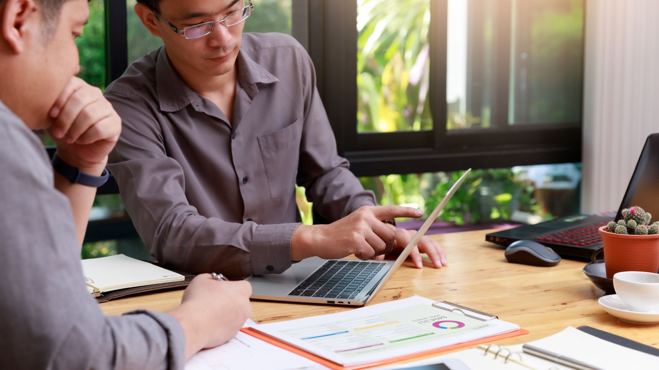 Dois profissionais em reunião analisando dados em um laptop e documentos sobre a mesa, representando tomada de decisão e uso de tecnologia em pequenas e médias empresas.